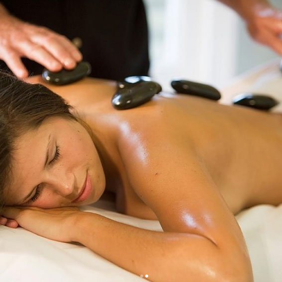 A women lying down relaxed on a massage table with hot stones on her back.
